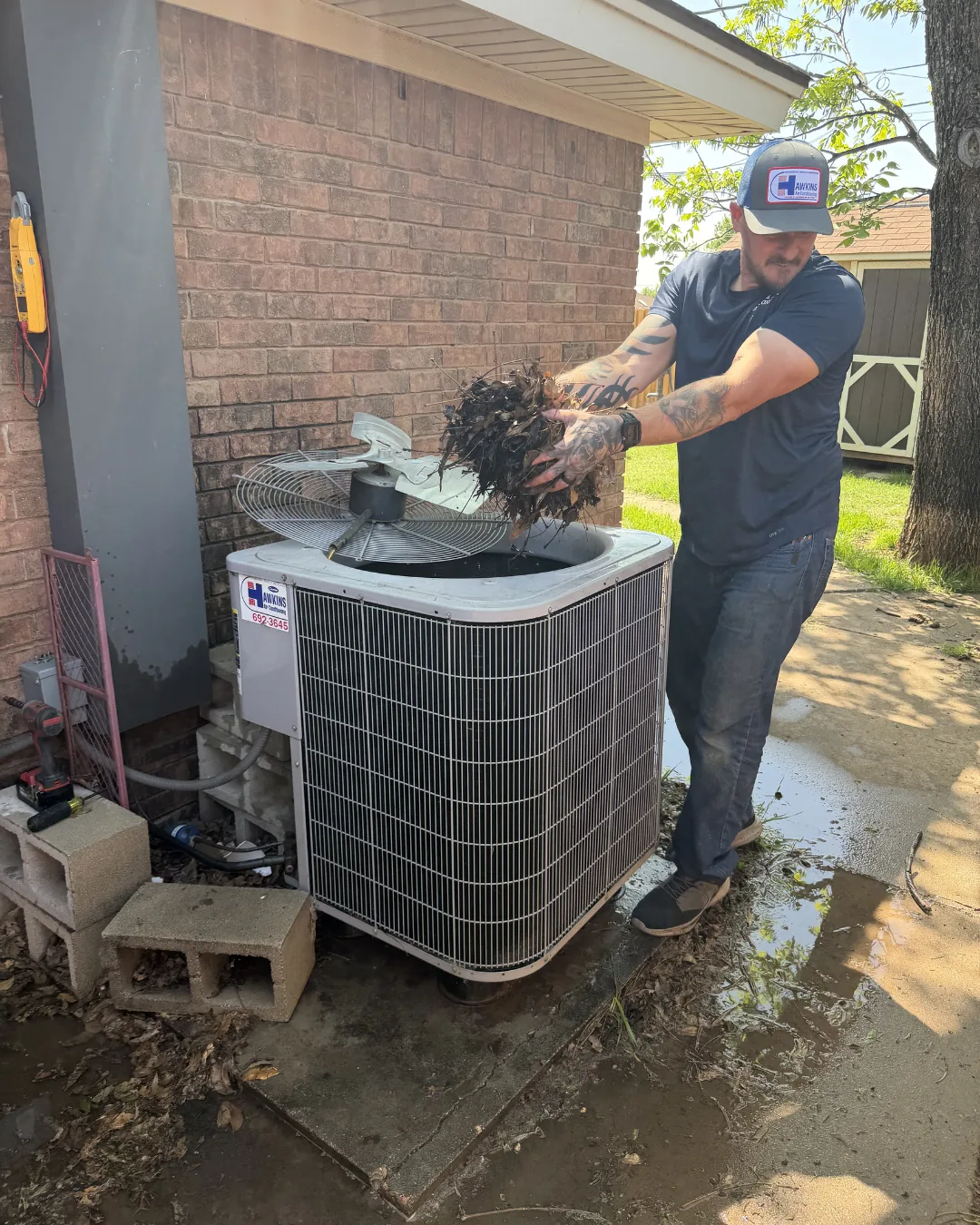 Hawkins technician clearing debris from an outdoor AC condenser on a service call in Abilene